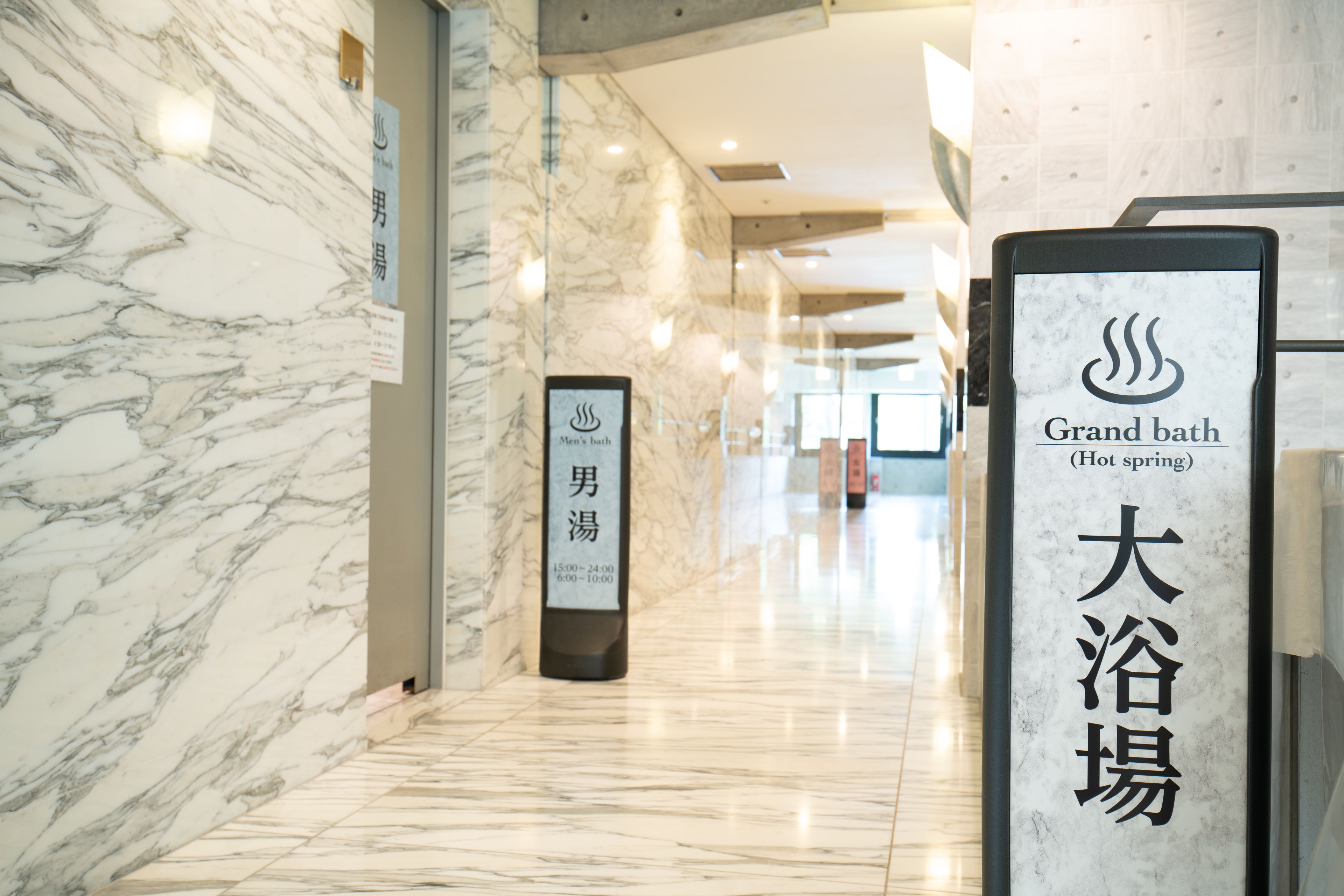A marble hallway with signs for 'Grand bath (Hot spring)' and 'Men's bath'.