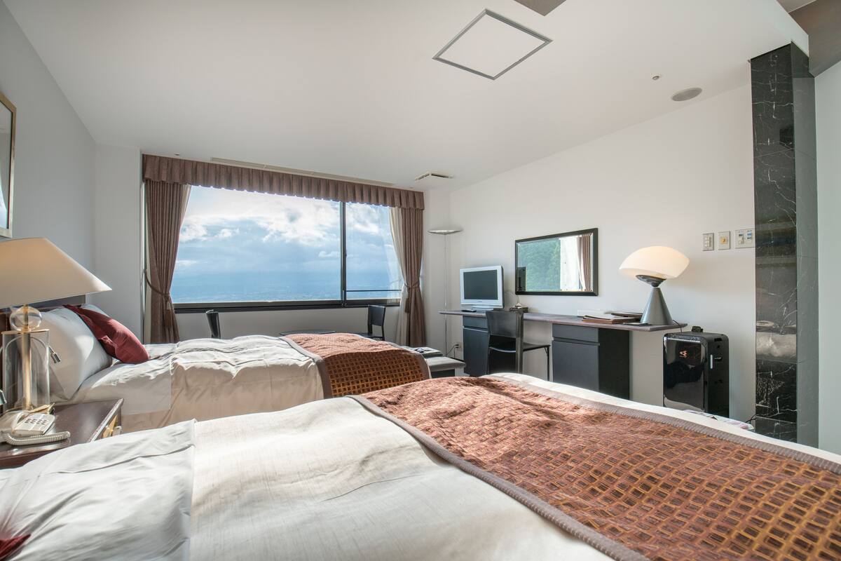 A hotel room with two beds, a desk, a computer, and a large window with a view.