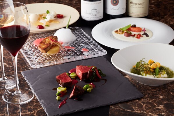 Una mesa de comedor con diferentes platos, copas de vino y botellas.