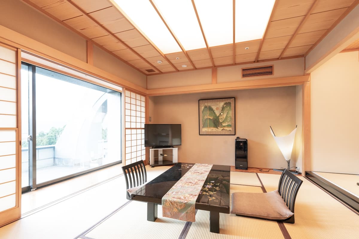 A traditional Japanese room with tatami flooring, a low table with a cushion, a television, and a painting on the wall.