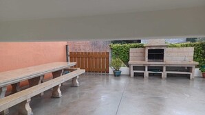 Un patio al aire libre con suelo de hormigón, un banco de madera, una parrilla y plantas en macetas.