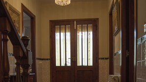 Un pasillo con escalera de madera, candelabro y puertas dobles con paneles de vidrio esmerilado.