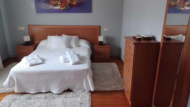 Un dormitorio ordenado con una cama grande, dos mesitas de noche con lámparas, un aparador de madera y un cuadro en la pared.