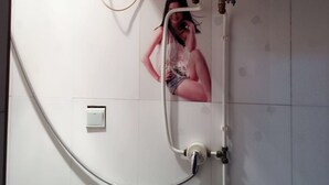 A bathroom with a white tiled wall, a white toilet, and a shower with a hose. - Huayang Guesthouse (Xianyang)