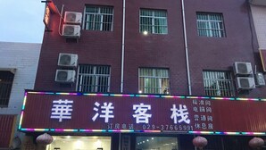 A hotel with a red facade, multiple air conditioning units, and a neon sign with Chinese characters. - Huayang Guesthouse (Xianyang)