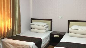 A hotel room with two beds, wooden flooring, and a patterned wall.