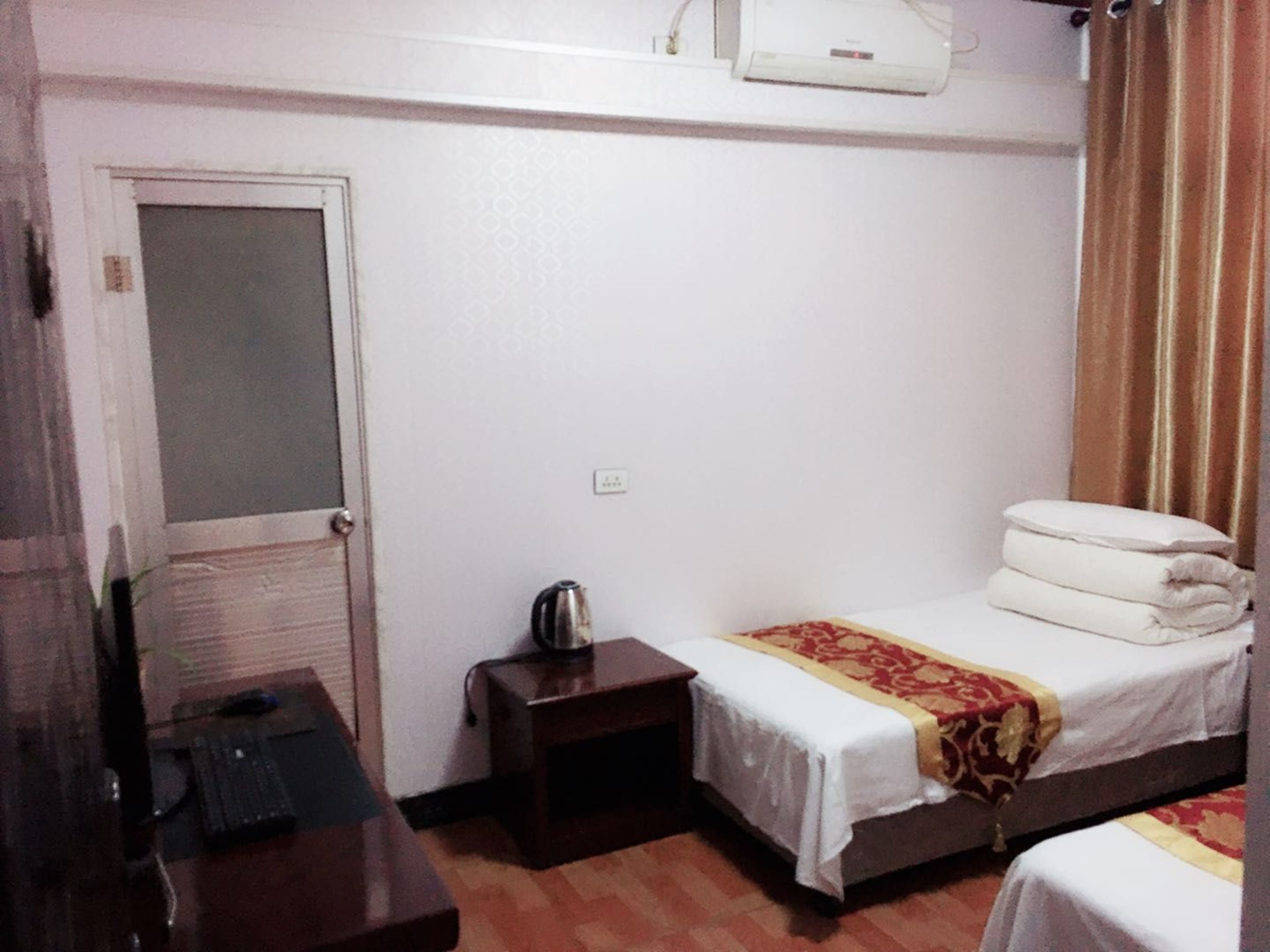 Habitación de hotel con una cama individual, un escritorio con una silla, una mesita con una tetera y un equipo de aire acondicionado en la pared.
