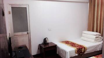 Habitación de hotel con una cama individual, un escritorio con una silla, una mesita con una tetera y un equipo de aire acondicionado en la pared.