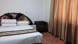 A hotel room with a bed, a small armchair, and a window with curtains. - Huayang Guesthouse (Xianyang)