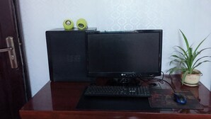 A wooden desk with a black monitor, keyboard, and mouse. There is a potted plant on the right side. - Huayang Guesthouse (Xianyang)