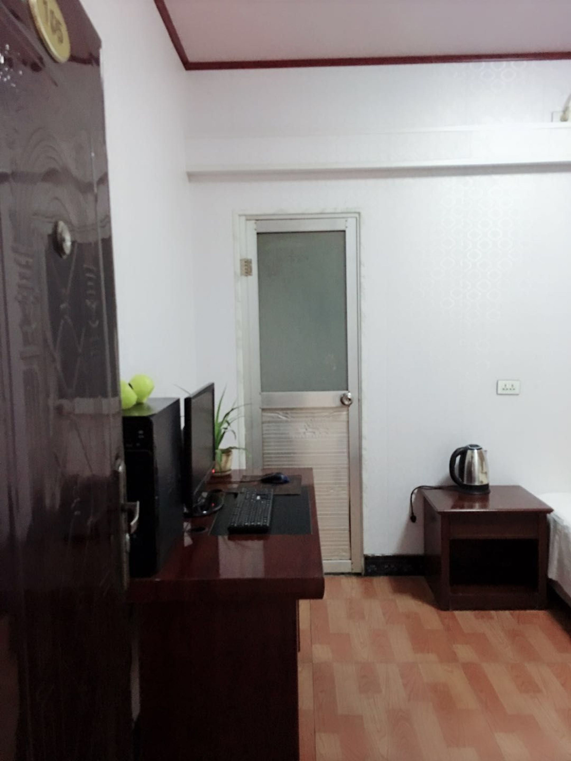A small room with a wooden desk, a computer, a plant, and a kettle on a side table.