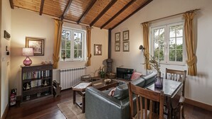 A cozy living room with a wooden ceiling, a fireplace, a sofa, a dining table, and a bookshelf. - Quinta Devónia - Cedro,country house with sea view (Funchal)