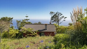 A house with a tiled roof surrounded by lush greenery and wildflowers. - Quinta Devónia - Cedro,country house with sea view (Funchal)