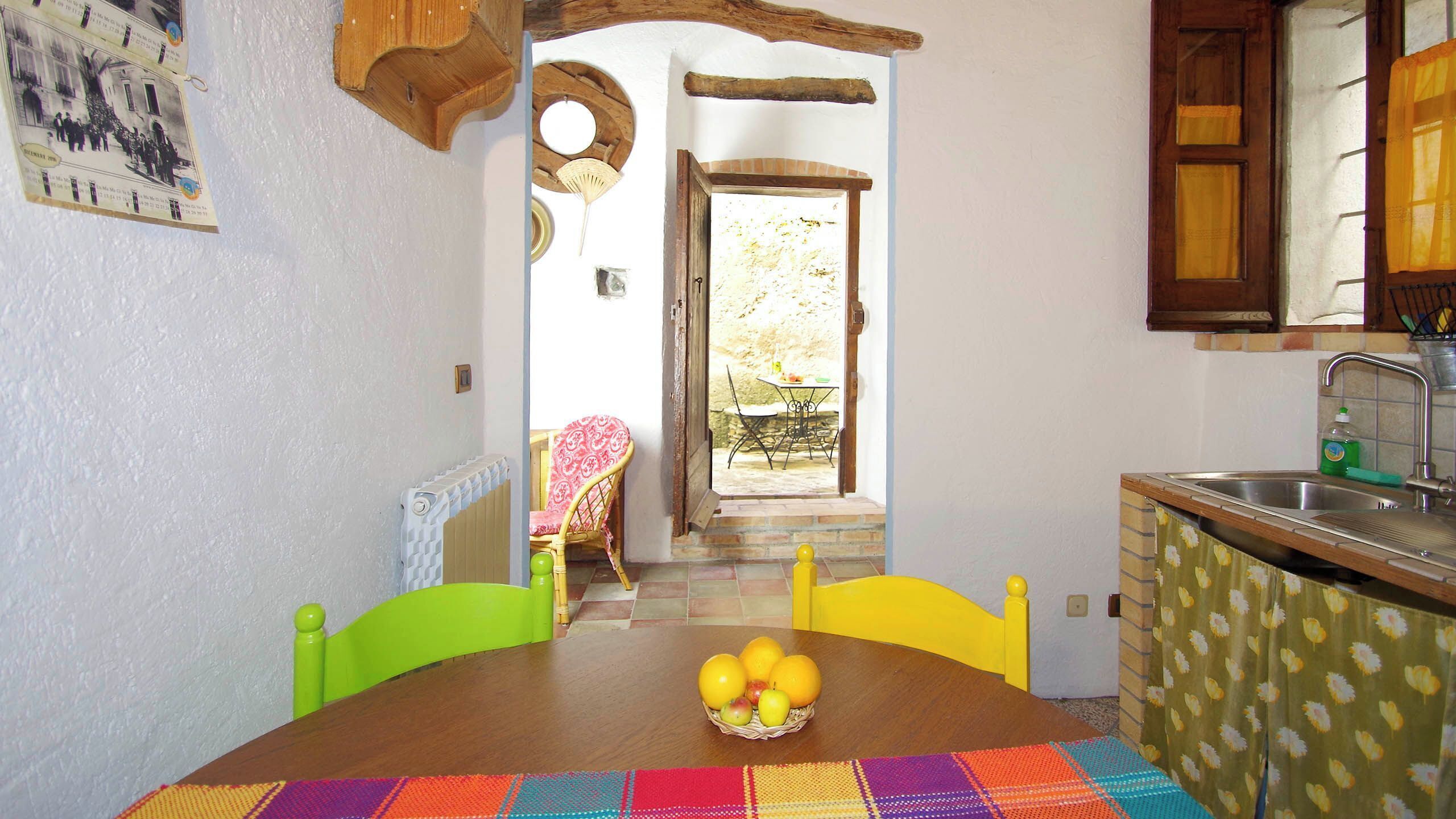 Een eetgedeelte met een tafel voor twee personen, een fruitmand en uitzicht op buiten.