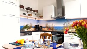 A modern kitchen with a coastal mural, white cabinets, and a wooden welcome sign. - *Anker Vacation Rental at Villa Victoria - GM 69836 - *Anker Vacation Rental at Villa Victoria (Graal-Müritz)
