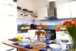 Una cocina moderna con un mural costero, armarios blancos y un letrero de bienvenida de madera.
