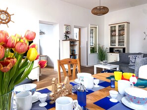 Una sala de estar con una mesa de madera dispuesta para el té, un sofá, una estantería y una rueda de barco decorativa.
