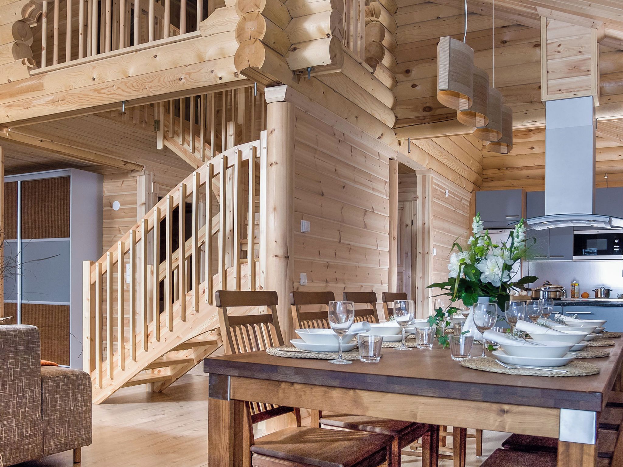 Un interior de madera con un comedor listo para una comida, una escalera y una cocina al fondo.