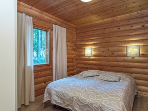 Een slaapkamer in een houten blokhut, met een bed, gordijnen en twee wandlampen.