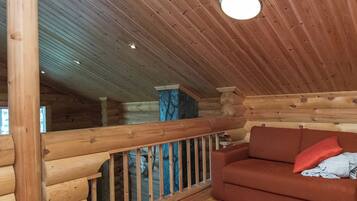 A log cabin interior with a wooden ceiling, a wooden railing, a red sofa, and a window.