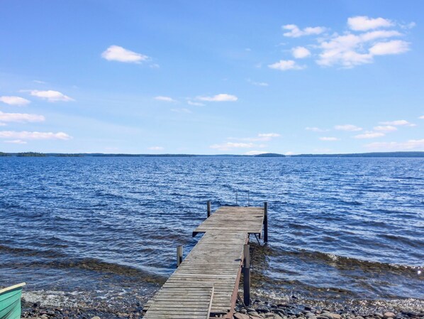 Eine hölzerne Pier, die sich in ruhiges Gewässer erstreckt, mit klarem Himmel darüber.