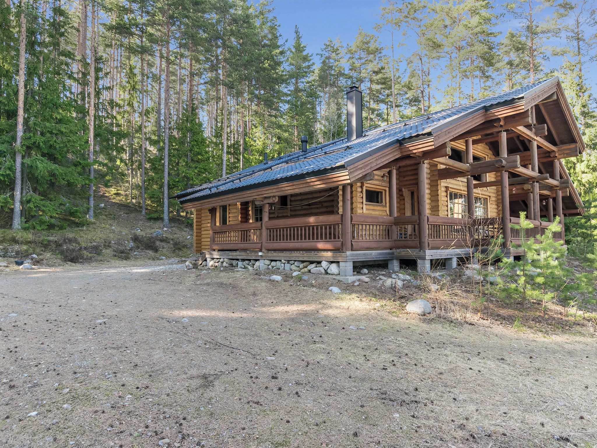 A log cabin with a porch, surrounded by a forest.