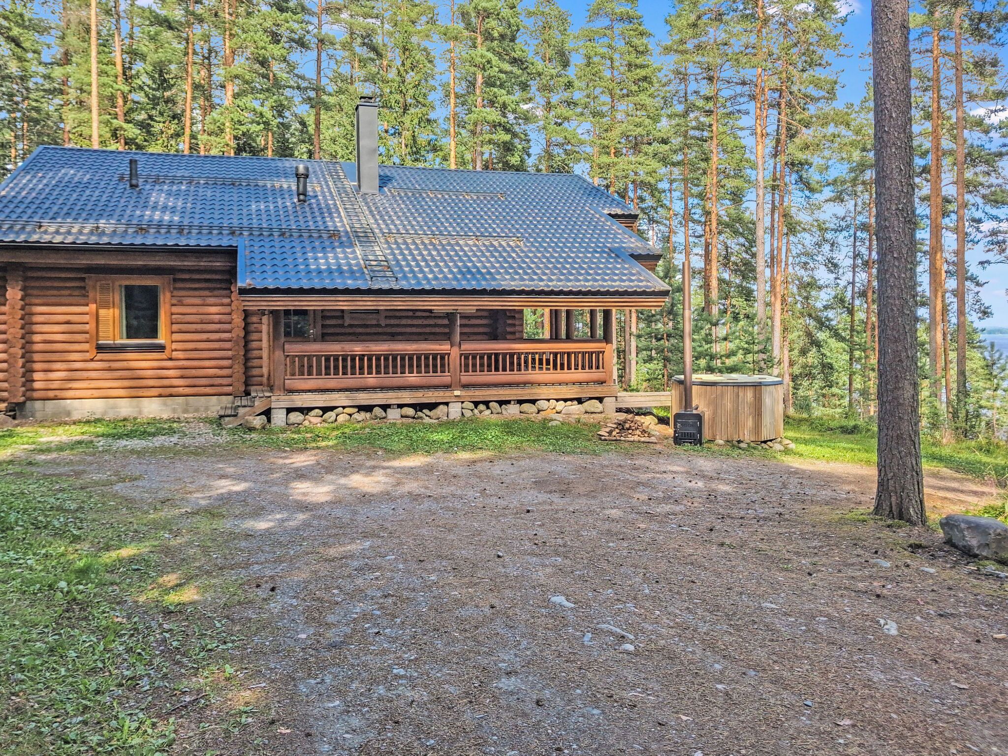 A log cabin with a porch, a chimney, and a view of a forest and water.