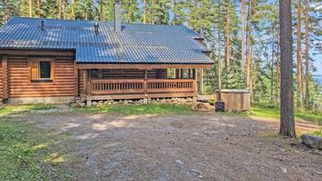 A log cabin with a porch, a chimney, and a view of a forest and water.