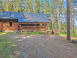 Eine Blockhütte mit Veranda, Schornstein und Blick auf Wald und Wasser.