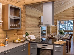 Een moderne keuken met houten wanden, een centraal eiland en een eethoek met uitzicht op bomen.