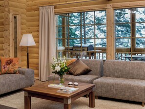 L’intérieur chaleureux d’un chalet en bois comprend un canapé, une table basse et une fenêtre donnant sur une forêt.