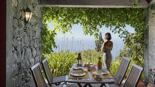 An outdoor dining area with stone walls, wooden furniture, and a view of the sea. - Quinta Devónia - Tília,country house with sea view (Funchal)