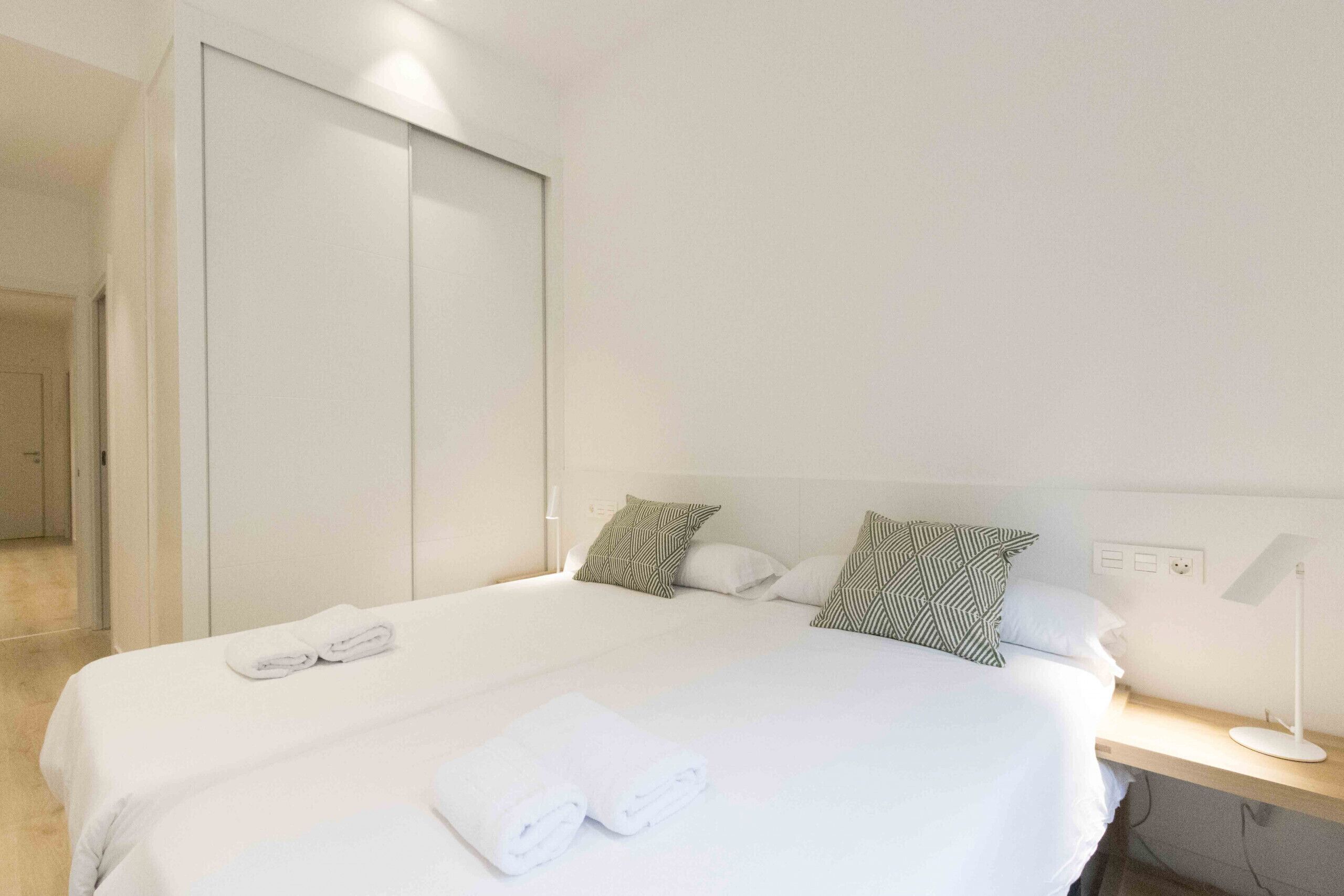A hotel room with a neatly made bed, a bedside table with a lamp, and a wardrobe.