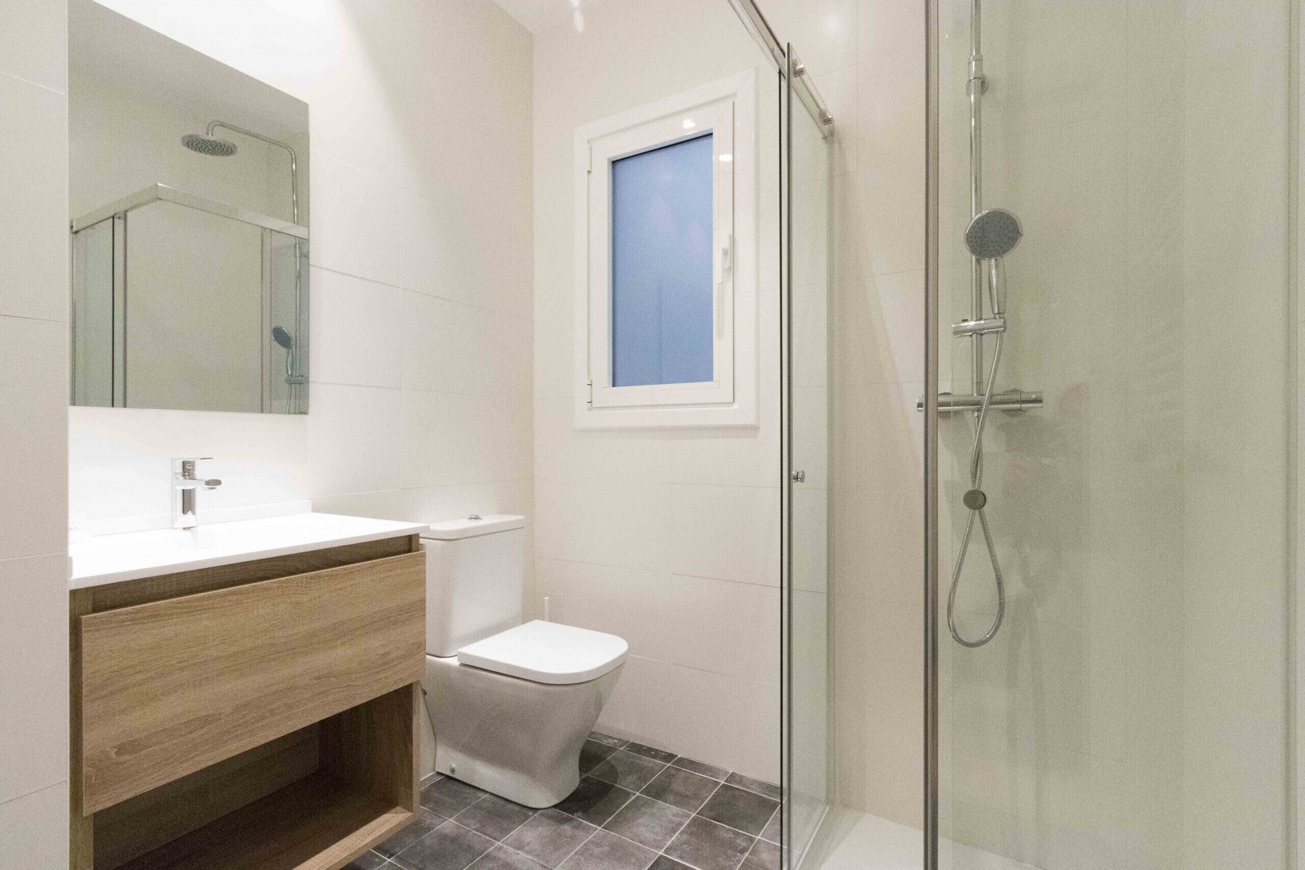 A modern bathroom with a glass-enclosed shower, a toilet, and a sink with a wooden vanity.