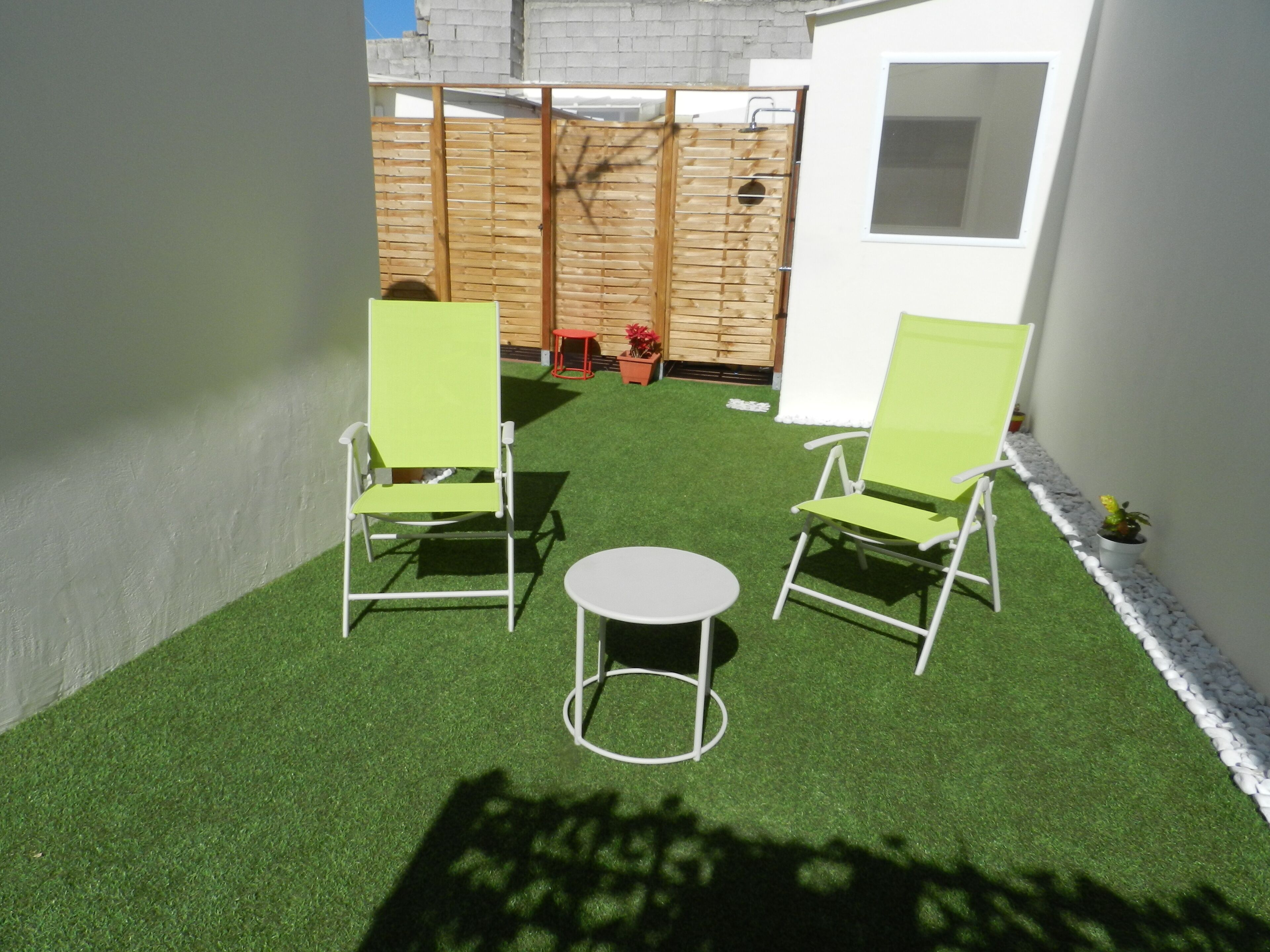 Eine kleine Terrasse mit zwei grünen Stühlen und einem runden Tisch, umgeben von Rasenteppich.