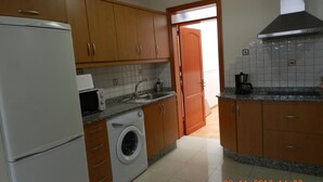 Une cuisine avec des meubles de rangement en bois, un lave-linge, un réfrigérateur, un four à micro-ondes et une machine à café.