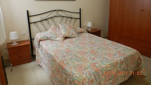 Une chambre à coucher avec un lit, une table de chevet, une lampe de chevet, une armoire en bois et un tableau accroché au mur.