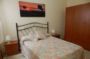 Ein Schlafzimmer mit einem Bett, einem Nachttisch, einer Nachttischlampe, einem Holzschrank und einem Bild an der Wand.