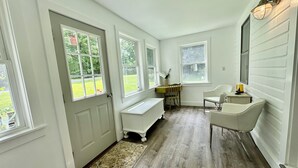 A room with a wooden floor, white walls, a bench, a desk, a chair, and a window with a view of greenery. - Spacious, Cozy 5 Bedroom Compound  (Saratoga Springs)