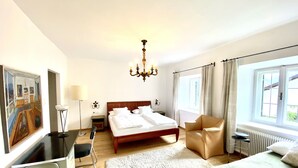 A hotel room with a bed, a chair, a desk, a lamp, a painting, and a window.