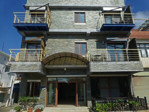 A multi-story building with a stone facade, balconies with railings, and a central entrance with a glass door.