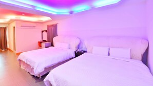 Hotellihuone, jossa on kaksi sänkyä, yöpöytä, peili ja värikkäästi valaistu katto.