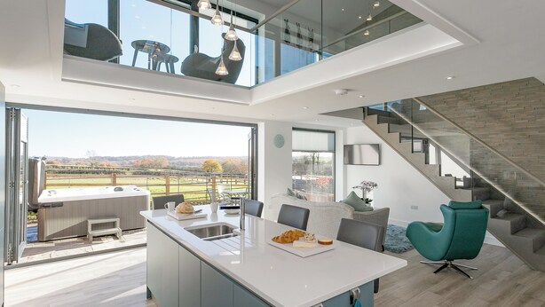Een moderne keuken met een centraal eiland, een zithoek met stoelen, een trap en uitzicht op het landschap.
