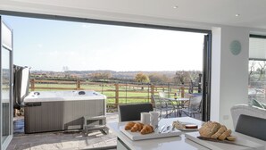 Een moderne keuken met een groot raam met uitzicht op een schilderachtig landschap, een bubbelbad en een ontbijt met croissants en kaas.