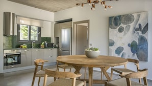 A modern kitchen with a round wooden table and six chairs, a large abstract painting on the wall, and a stainless steel refrigerator. - Villa Lantana is perfect for guests wishing to have a peaceful and pleasant stay (Skala)