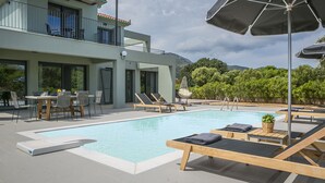 A modern pool area with lounge chairs, a table, and umbrellas. - Villa Lantana is perfect for guests wishing to have a peaceful and pleasant stay (Skala)