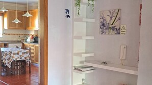Un salon avec un tapis à motifs, une étagère blanche ornée de plantes, un tableau et un vase rempli de fleurs.