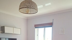 Un salon comprenant une télévision, une table avec un saladier, une chaise, un canapé et un luminaire suspendu.