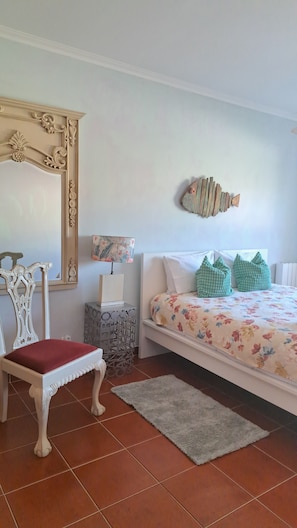 A bedroom with a bed, a chair, a nightstand, a lamp, a decorative fish wall art, and a floral bedspread. - Camarção Violante apartment Lagoa  (Foz do Arelho)