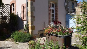 Un patio con un muro de piedra, una puerta de metal y un cantero con diversas plantas y flores.